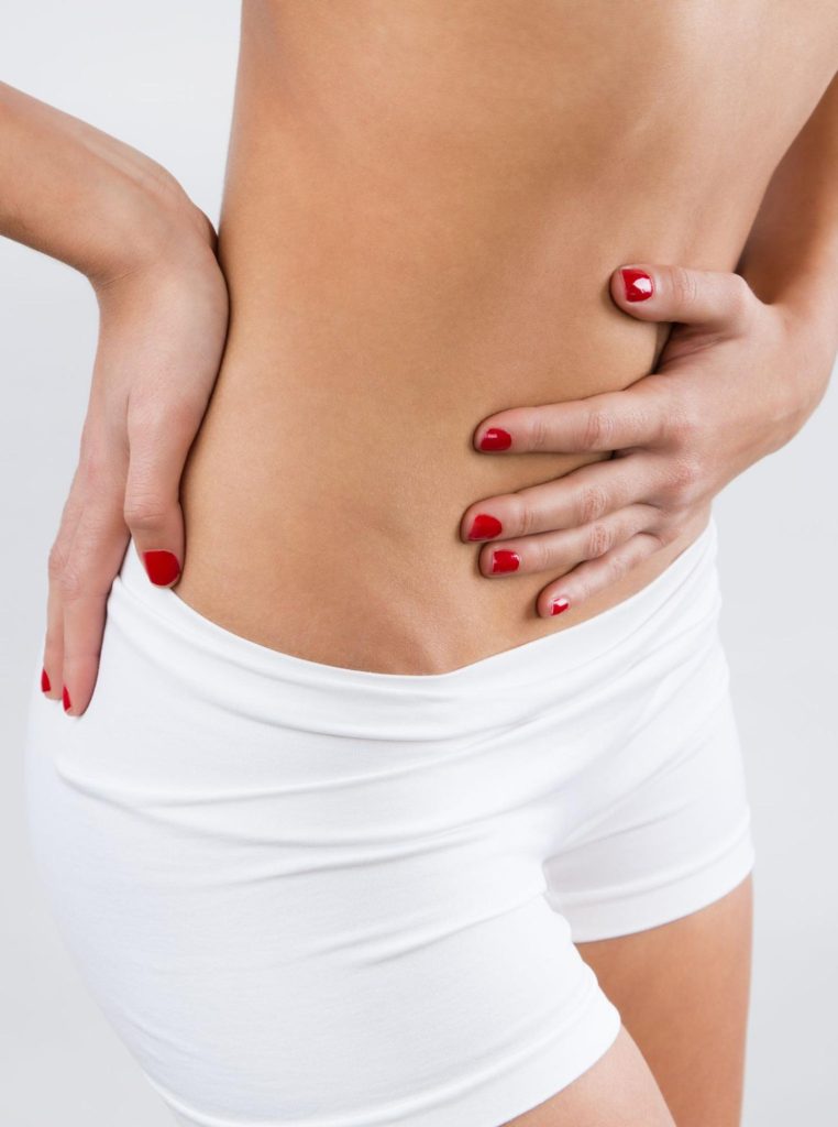 жена в бяло бельо и червени нокти се държи за кръста и корема