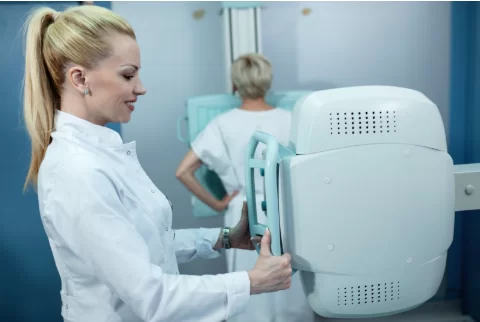 Усмихната медицинска сестра прави рентгенова снимка на пациентка.