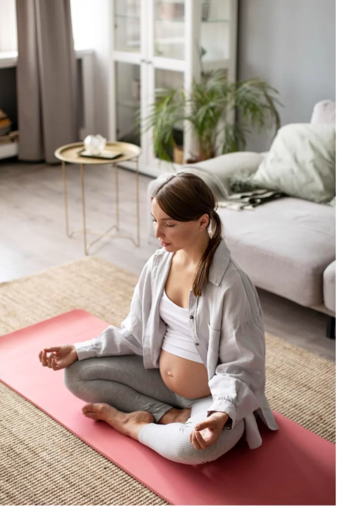 Бременна жена практикува йога, седнала на пода у дома си.
