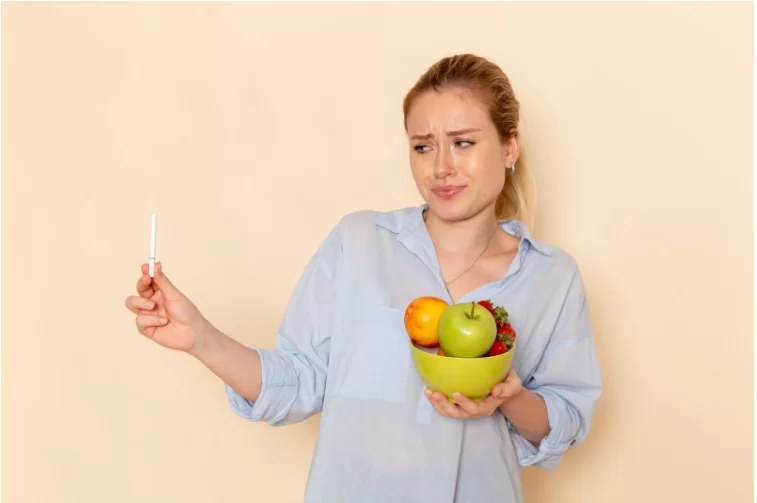 Бременна жена държи в едната ръка купа с плодове и гледа намръщено към цигара в другата ръка.