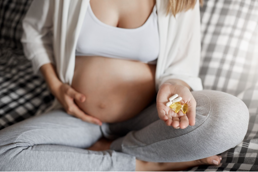 Бременна жена е седнала на диван и държи в шепата си хапчета.